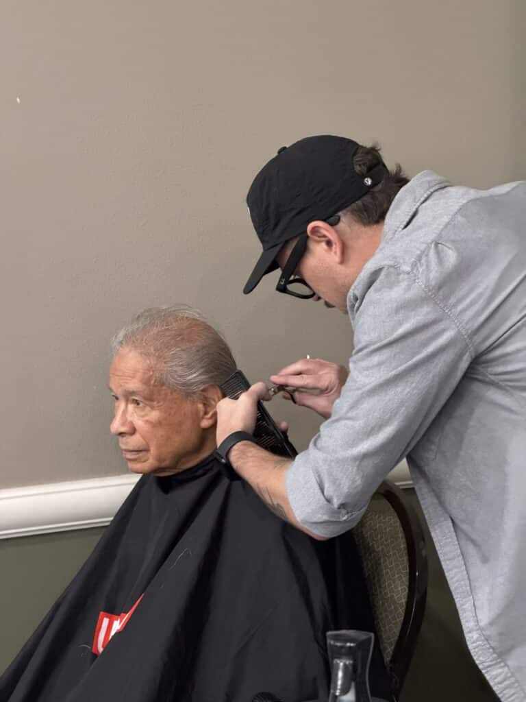 Man in a cap cutting a seated man's hair