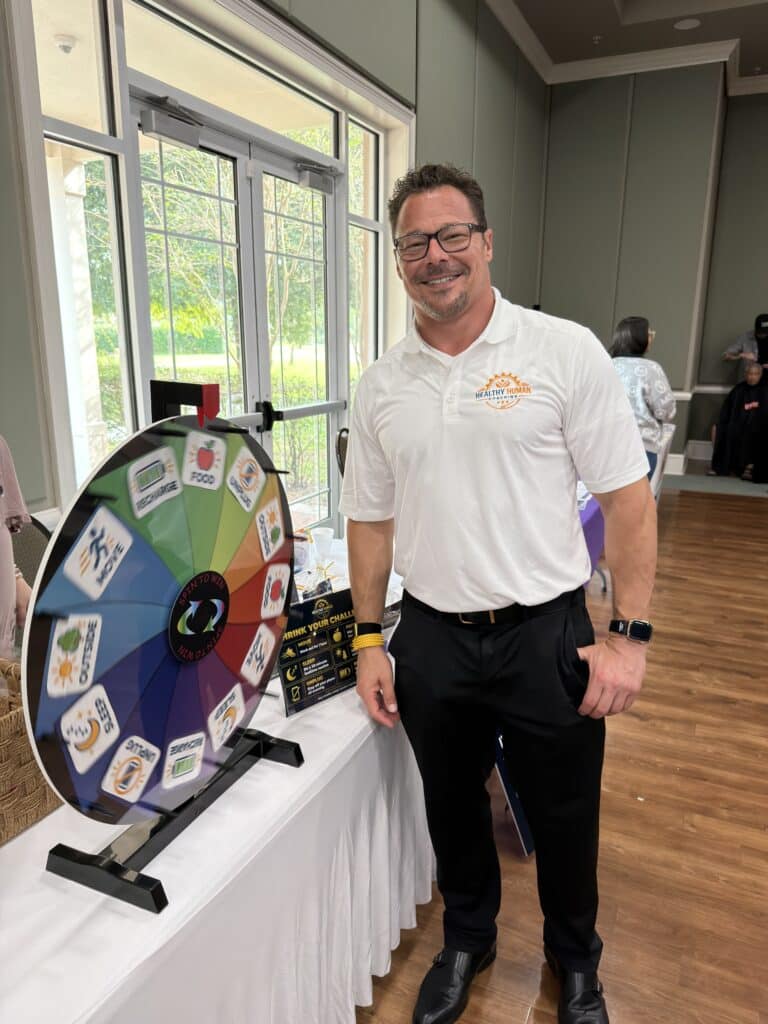 Man in a white polo smiling beside a prize wheel