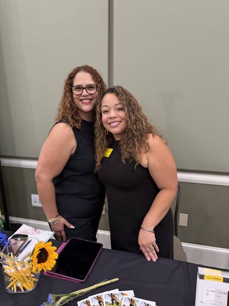 Two women smiling together behind a vendor table